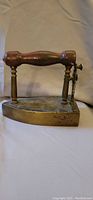 Side view of antique cast iron iron showing wooden handle and metal lever mechanism