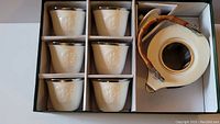 Overview of tea set in original packaging showing six cups and one teapot with bamboo handle.