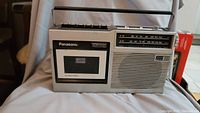 Front view of the entire Panasonic cassette radio showing speaker, cassette slot, radio tuner, and control buttons on top.