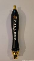 Full view of black Sapporo beer tap handle with gold top and bottom and white lettering with gold star.