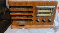 Side angle photo showing wood finish, speaker grille, tuning knobs, frequency display, and Thomas brand label.