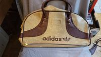 Wide view of the vintage Adidas sports bag showing leather-like handles, beige body with brown accents, and Adidas logo on front.