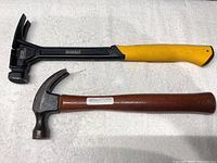 Photo showing two claw hammers placed side by side: one DeWalt model with yellow and black handle, the other traditional wooden handled hammer.