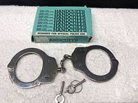 Full view of nickel plated steel handcuffs with connecting chain, two included keys, and original box.