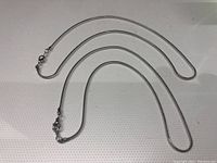 Two silver-colored snake chain necklaces laid flat on a white background.