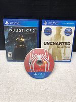 Photo showing Injustice 2 and Uncharted PS4 game cases standing upright and Spider-Man game disc laying flat in front