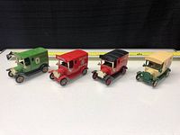 Front and side view of four Lledo die-cast beer delivery trucks aligned side by side, showcasing different colors and branding.