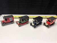 Four vintage style Lledo beer delivery trucks aligned front-facing with a measuring tape behind showing roughly 4 inch length.