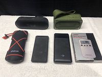 Lot of Bluetooth speakers and accessories unpacked and displayed on a white towel backdrop