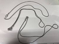 Three silver-toned chain necklaces laid flat to show overall styles and lengths
