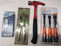 Photo showing full lot with all items: stapling pliers, leather punch pliers, hammer, and wood chisel set.