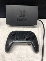 Nintendo Switch Dock with Nintendo Switch Pro Controller in front on a white surface