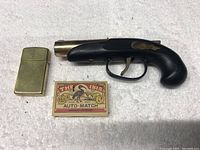 Top view photo showing the brass Zippo lighter, pistol-shaped lighter, and The Ibis matchbox together.