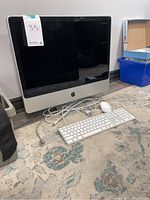 Front view of Apple iMac desktop computer with keyboard and mouse on carpeted floor, cables attached and loose.