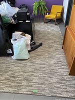 Photo showing the full view of the 10x12 gray and white area rug in a room, partially covered by furniture items including a yellow rocking chair.
