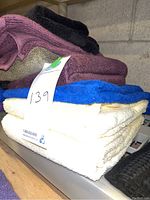 Stack of assorted bath towels in purple, cream, blue, maroon, black, and olive green colors with a lot tag visible.