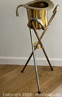 Front view of brass top hat-shaped ice bucket resting on three cane stand showing overall design and condition.