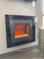 Electric firebox showing a different flame effect setting with orange glow inside black frame and white stones at base.