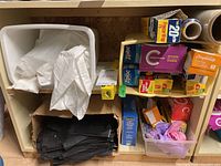 View of assorted white and black garbage bags in and on a shelving unit alongside boxed plastic wrap and bags.