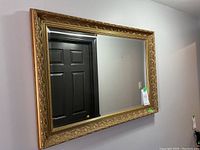 Full view of the rectangular gilded mirror hanging on the wall showing the full frame and glass surface.