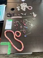 Assortment of costume jewelry including necklaces, bracelets, rings, earrings, and pendants displayed on a dark wooden table.