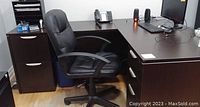 L-shaped desk with built-in drawers on both sides and black leather office chair positioned in front of desk