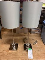 Two 30-inch tall table lamps with white shades and silver bases on wooden floor