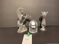 Three lead crystal items including rearing horse figurine, clock, and candle holder arranged side by side against a dark background.