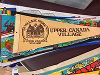 Beige fabric pennant for Upper Canada Village featuring a black graphic of a village store and text.