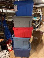 Stacked five assorted plastic storage bins in different colors in a basement or storage area.