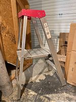 Side view of the 4-step aluminum folding step ladder with red top platform showing steps and frame.