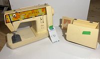 Full view of vintage Singer Genie sewing machine with beige hard case and manuals placed alongside it.