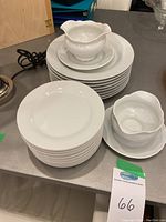 Photo showing stacked white dinner plates, smaller plates, a gravy boat with attached underplate and sugar bowl with underplate on a grey surface.