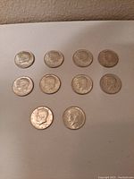 Obverse side of ten 1964-D Kennedy half dollar coins showing the profile of President John F. Kennedy. Coins show wear and tarnish.