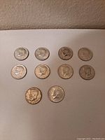 Ten 1967 Kennedy half dollar coins laid out on a flat surface showing the obverse side with JFK profile.