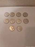 Obverse view of ten Kennedy half dollar coins arranged in two rows showing the profile of President John F. Kennedy with visible wear and tarnish.