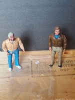 Two A-Team action figures on a wooden surface with a black background