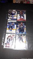 Photo showing six signed NHL hockey cards in plastic sheet protector laid on black surface.