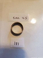 Photo of silver ring placed on a white paper background with handwritten label showing 'Size 4.5' and lot number 181.