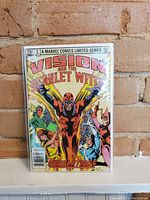 Front cover of Vision and the Scarlet Witch #4 comic showing the title, main characters, and price of 75 cents. The comic is held against a brick wall background.