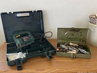 Bosch PST 50E jigsaw inside green plastic carrying case next to Piper cutter kit in green metal box on wooden table.