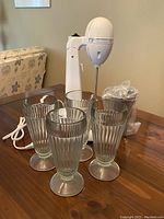 Classic Hamilton Beach Drink Master milkshake mixer appliance with four clear ribbed dessert cups arranged in front on a wooden table.