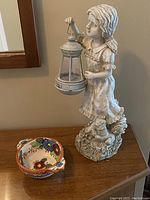 Photo of decorative girl statue lamp holding lantern and hand-painted floral bowl on wooden surface