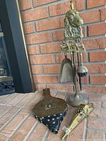 Full view of the fireplace tool stand with attached fireplace tools, bellows, and match holder displayed against a brick background.