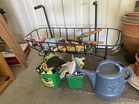 Overview of gardening tools including metal garden kneeler frame, gloves, watering can, pruning shears and plastic containers.