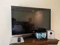Front view of LG flat screen LCD TV with remote control and blue and white external speakers on the cabinet.