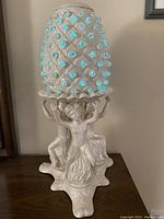 Front side of the lamp showing three cherubs holding a pineapple-shaped shade with blue lights glowing through the knobs.