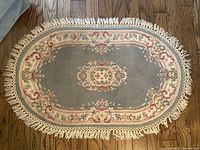 Full top-view of blue oval floral area rug with white fringes laid on wooden floor.