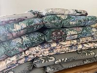 Stacked patio chair cushions showing multiple floral and botanical designs in various colors and patterns