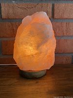 Full view of the lit salt rock lamp showing the natural pink-orange salt crystal glowing warmly on a wooden base.
